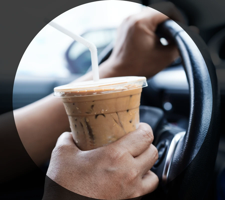 A Car Driver Holds a Drink While Driving a Car